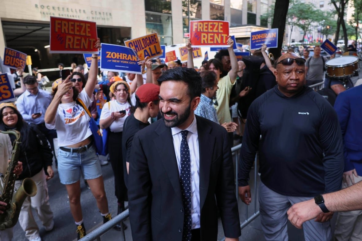 Zohran mamdani smiling among supporters on city streets.