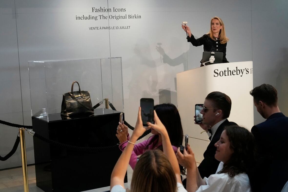 Auctioneer presenting original Birkin handbag inside glass case