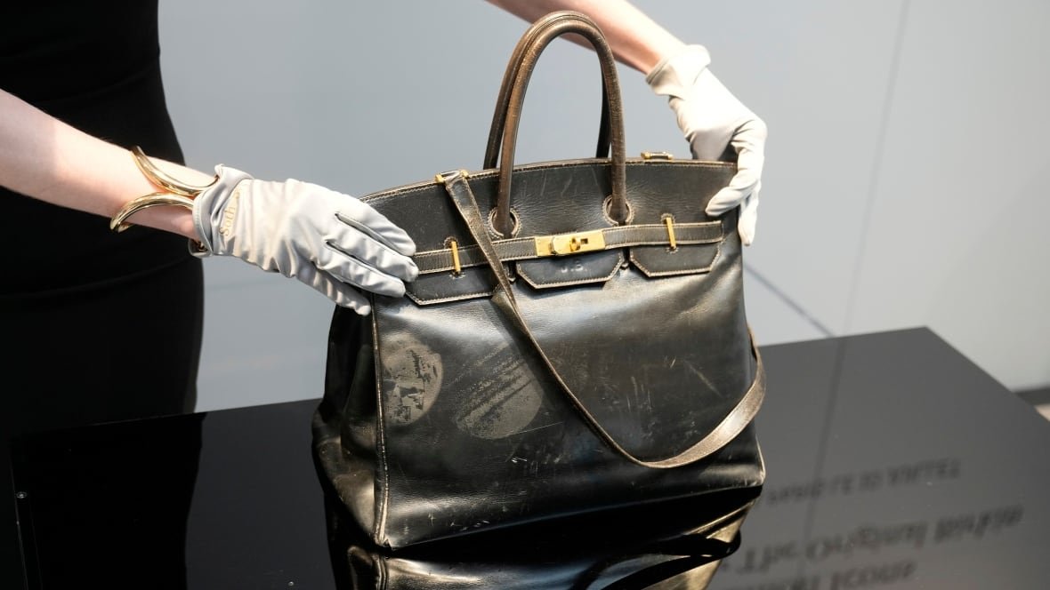 Auctioneer presenting original black leather Birkin bag inside glass case