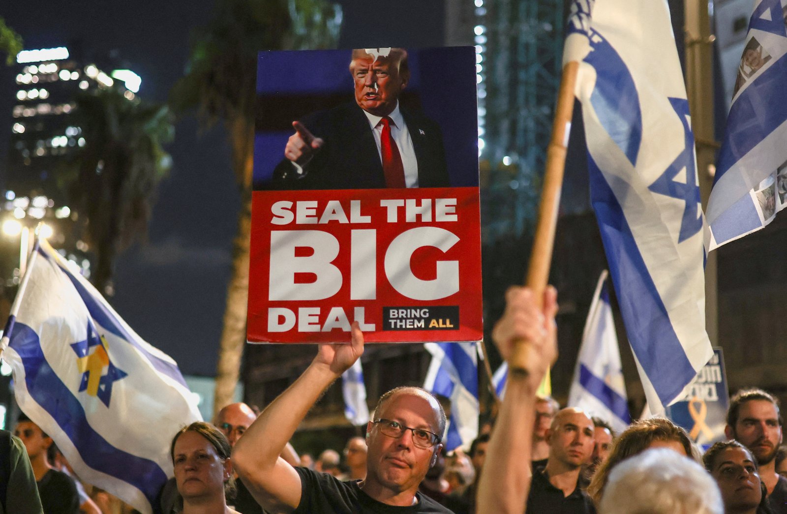 Protester holding sign depicting US President Donald Trump alongside Israeli flags at rally demanding end to war in Gaza