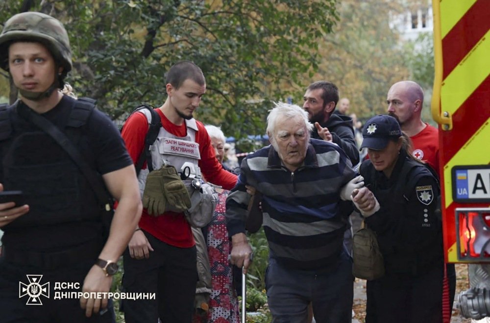 Ukrainian emergency responders assisting an elderly individual after a drone strike near residential buildings in Dnipro.