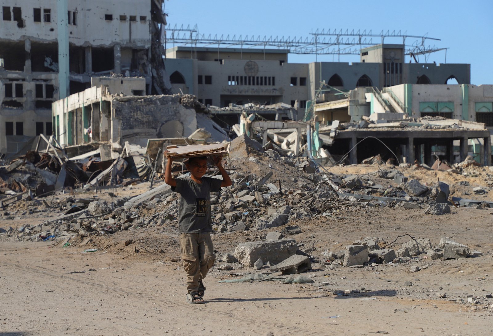 A Palestinian boy walks carrying a piece of wood board through the wreckage of Gaza City, October 16, 2025. [ebrahim Hajjaj/Reuters]