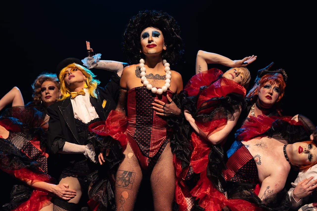 Drag performers surrounding Shelita Cox dressed vibrantly.
