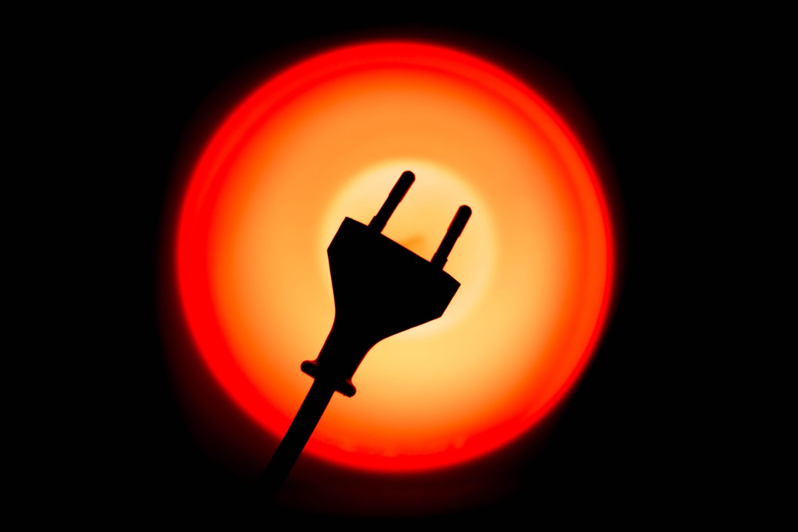 Close-up image showing an electric plug positioned before a glowing red lamp.