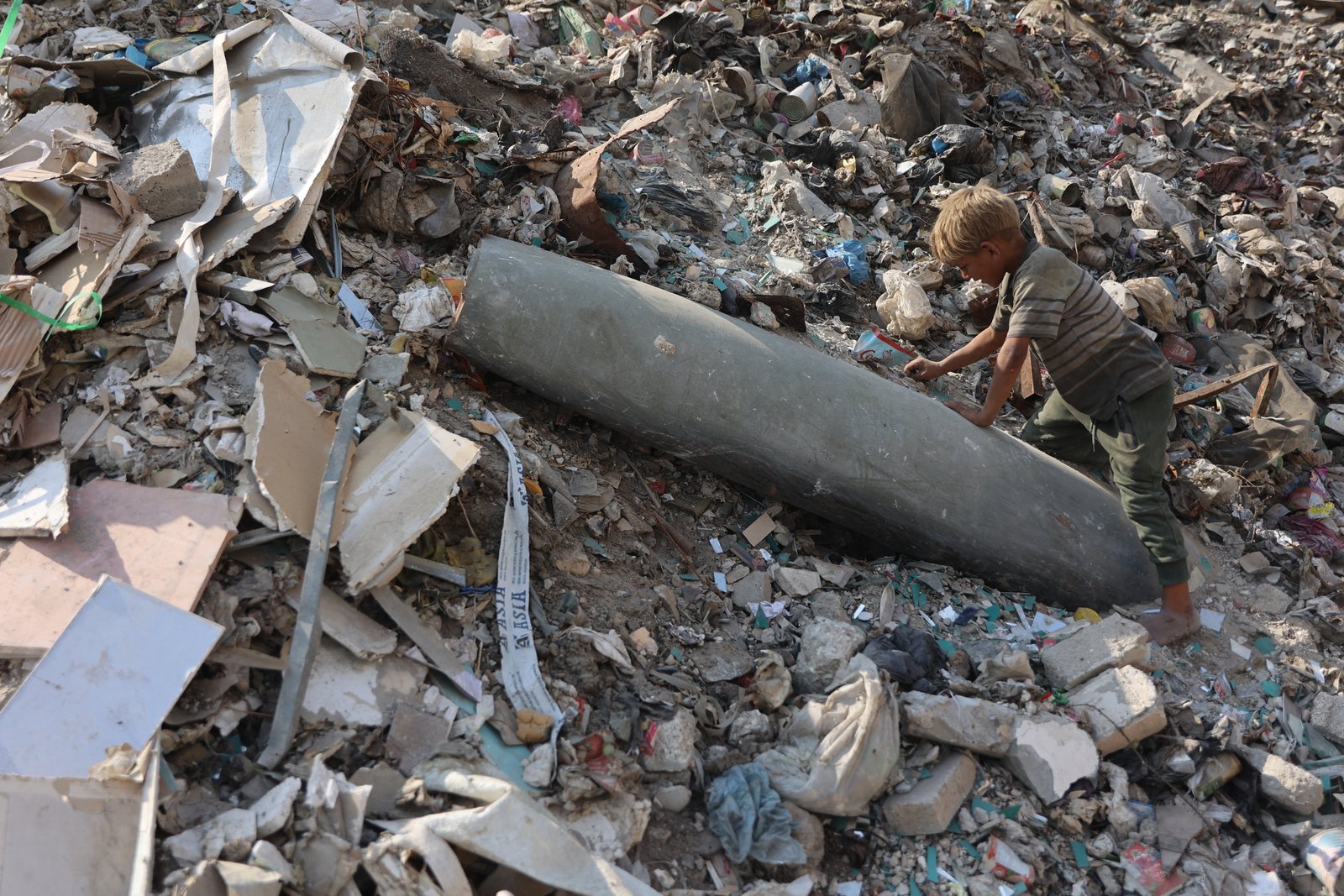 A Palestinian child examines an unexploded missile at a waste site in Firas market area, Gaza City
