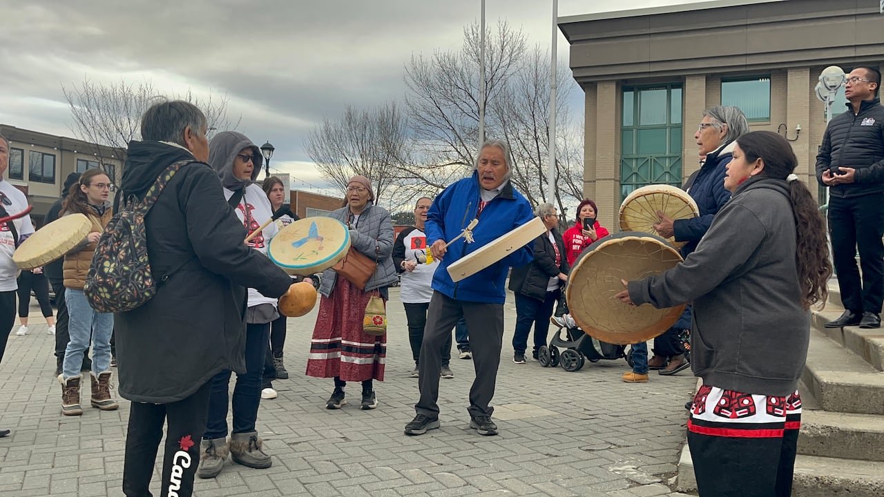 Community members gather outside courthouse holding drums