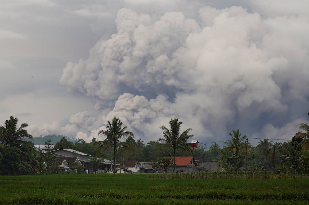 Volcanic ash clouds rising behind houses near Mount semeru