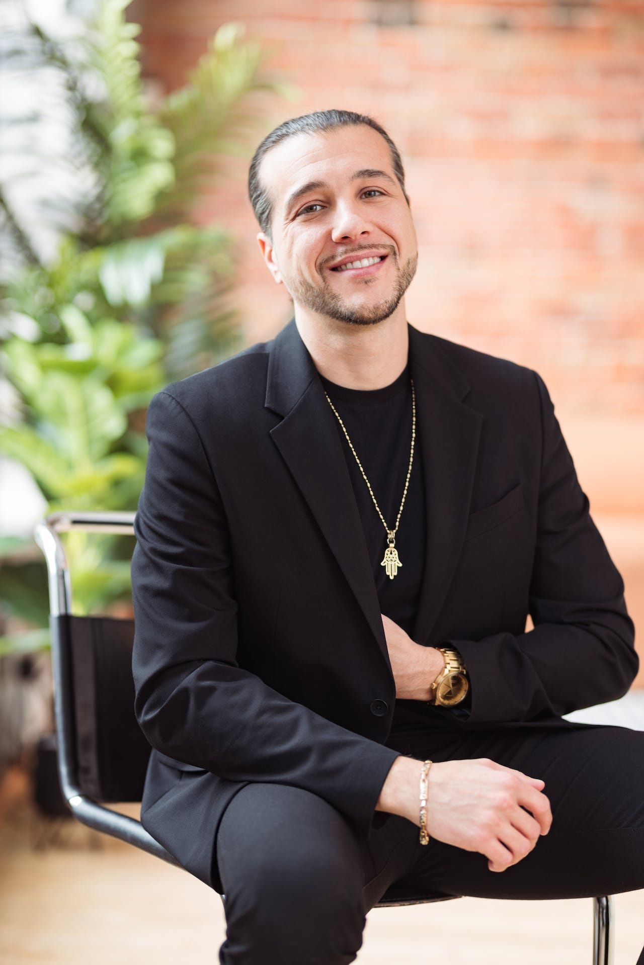 Karim S.Leduc seated smiling against brick wall backdrop