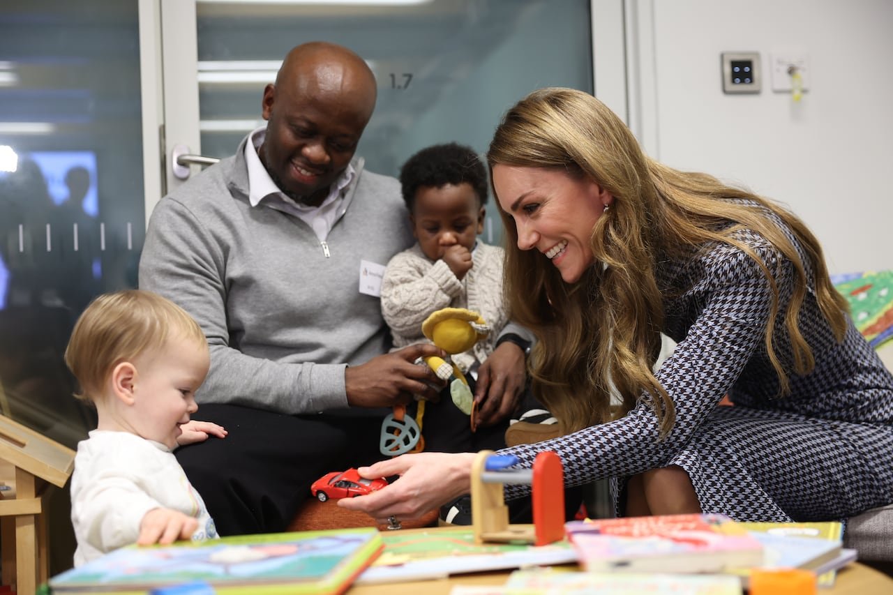 An adult handing a toy car to a child while others watch nearby.