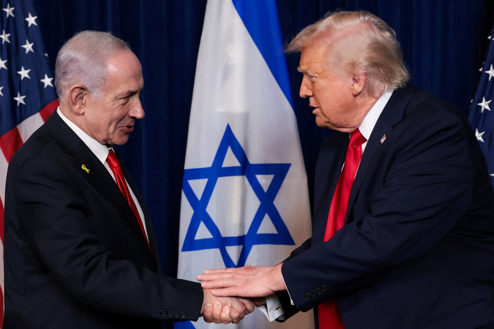 Benjamin Netanyahu shaking hands with Donald Trump against backdrop of Israeli flag