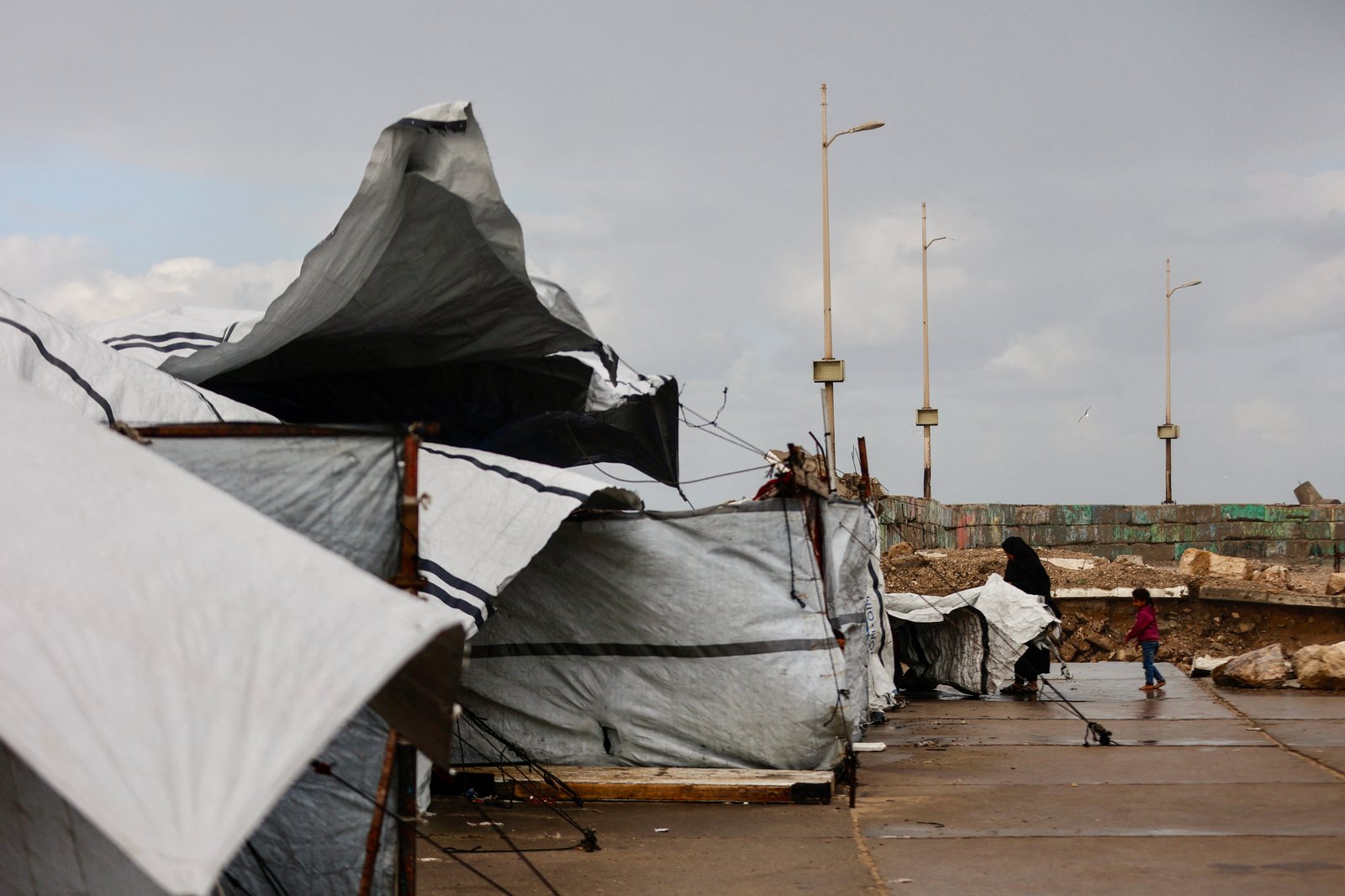 Displaced Palestinian woman securing family tent amid winter rains in Gaza City