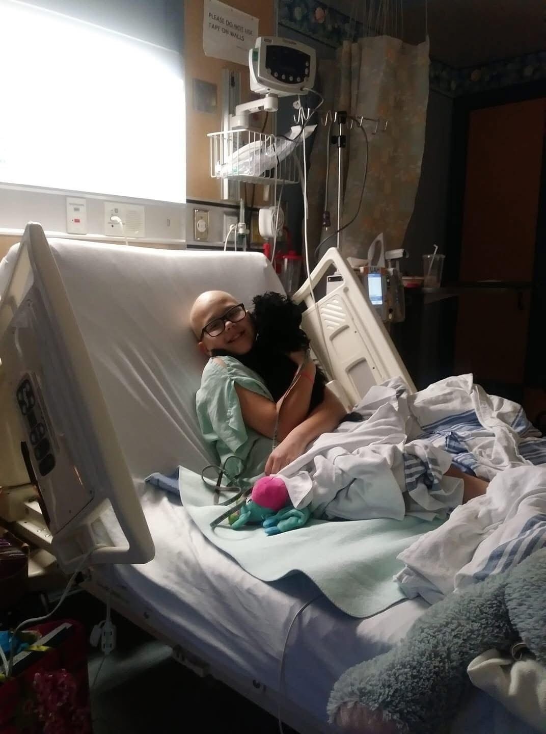 A child clutching a stuffed animal while resting in a hospital bed