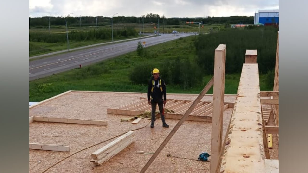 Construction worker wearing helmet standing atop building frame.