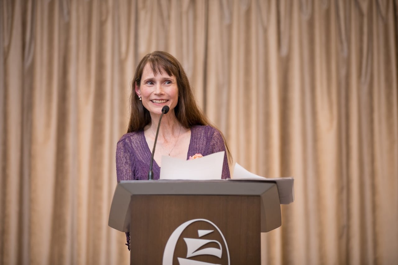Two elegantly dressed women reading aloud at podium