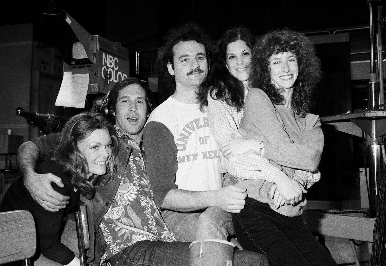 Black-and-white photo featuring original saturday Night Live cast members including Chevy chase smiling together