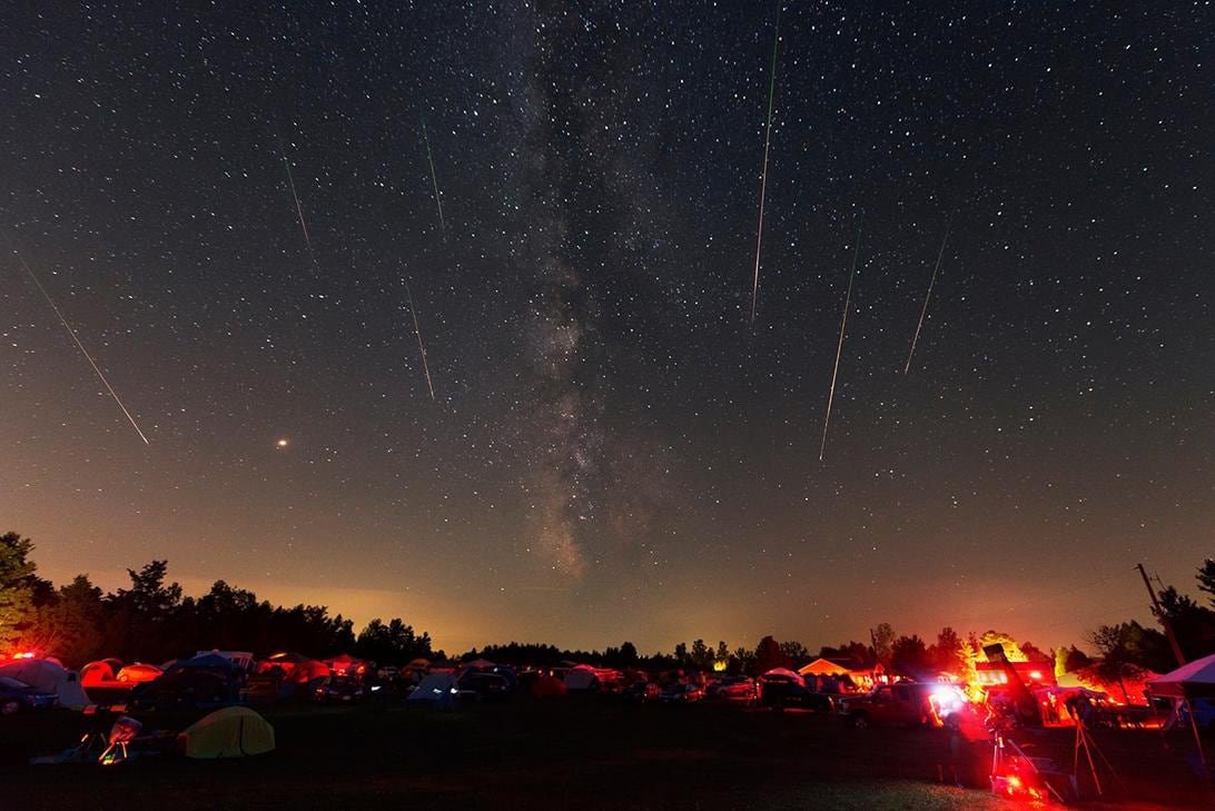 Bright Perseid meteors streaking across a clear night sky over desert terrain.