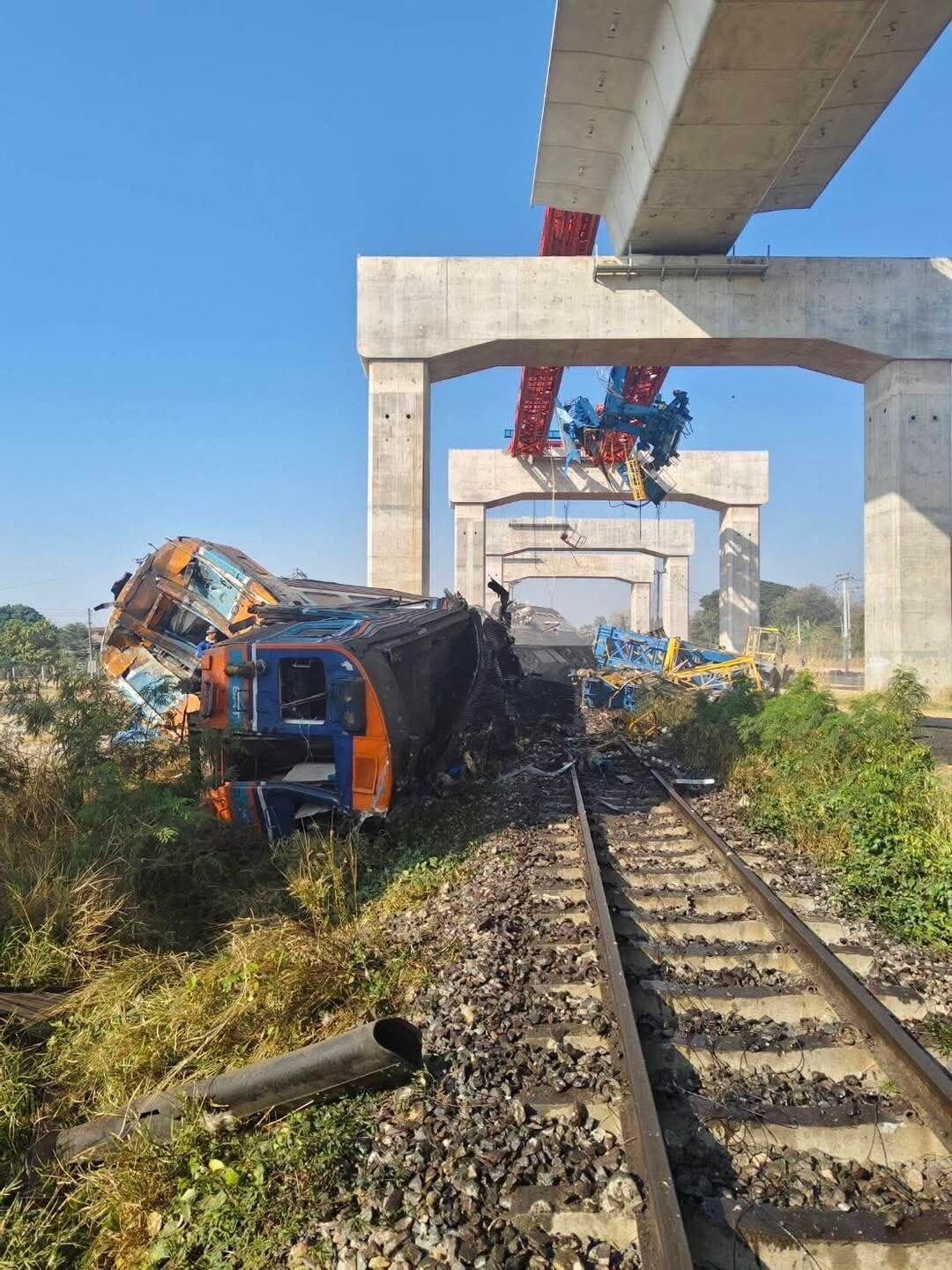 A derailed passenger train car lies crumpled on its side beside railway tracks