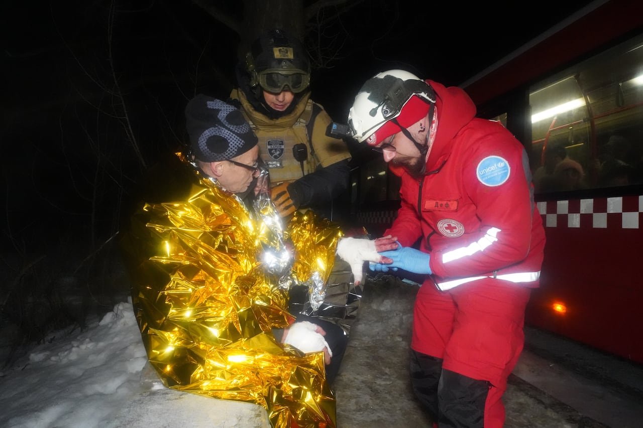 Paramedic treating an injured man wrapped in thermal blanket during Russian airstrike aftermath