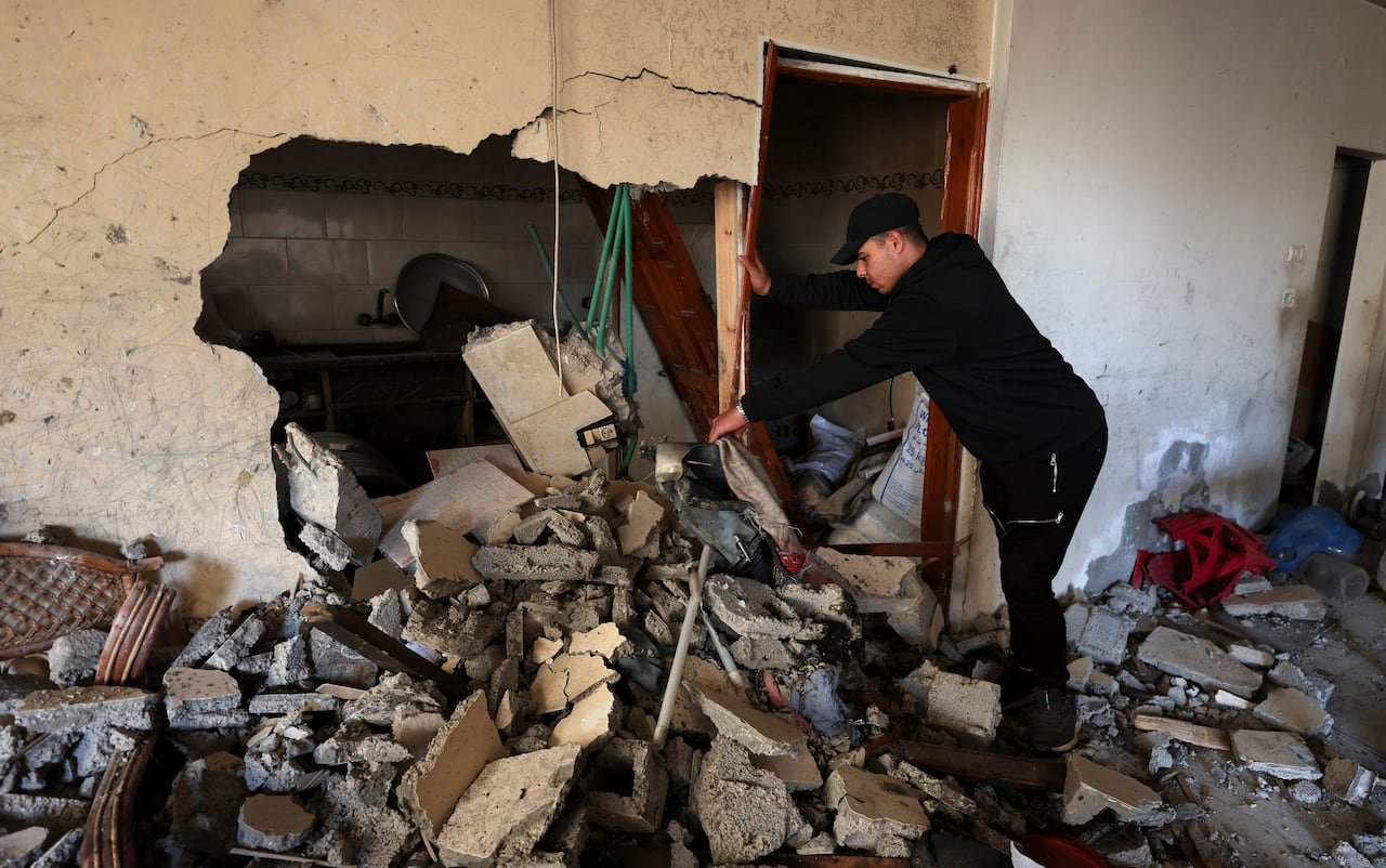 Young man standing atop rubble surveying destruction inside damaged apartment.