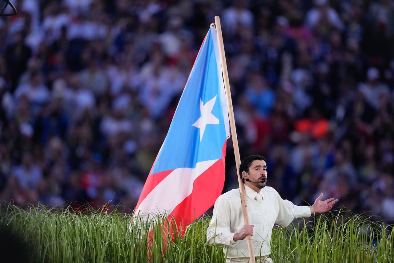 Bad Bunny performs carrying large light blue triangle puerto rican flag trailing behind him