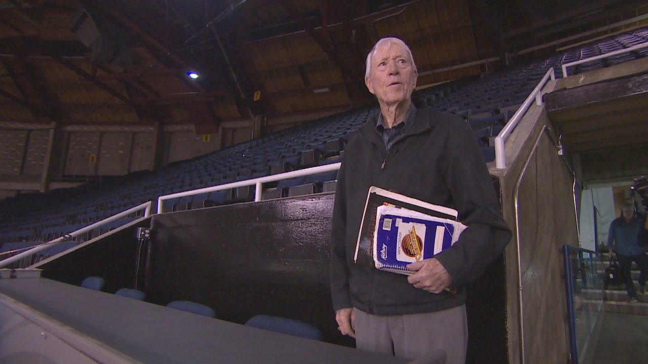 Jim robson standing inside an arena holding a notebook featuring Vancouver Canucks imagery