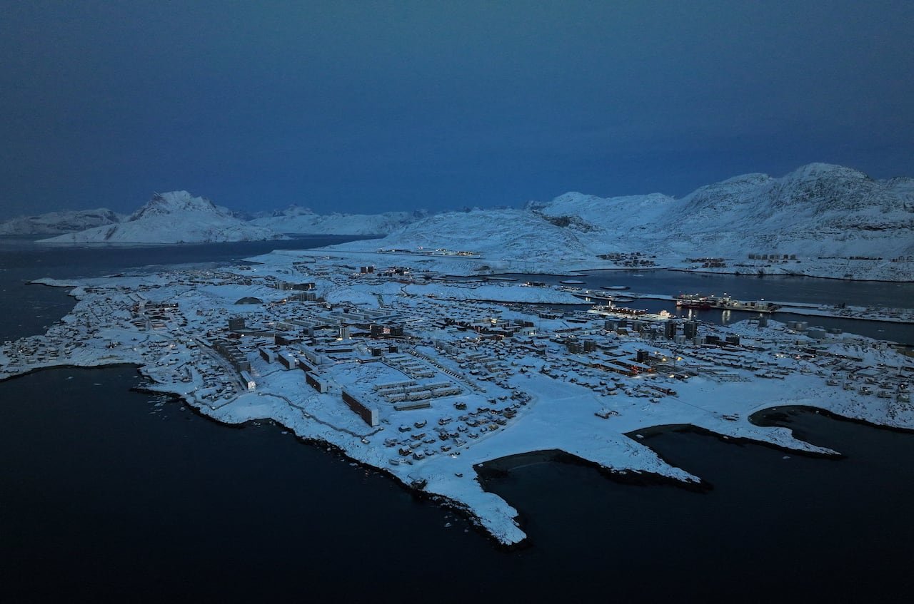 Nighttime aerial view showing Nuuk city lights surrounded by icy fjords.