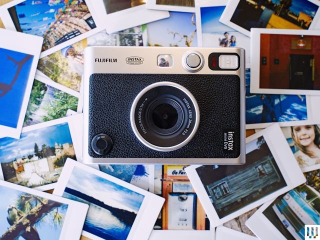 Overhead view of a Fujifilm Instax Mini Evo black and silver camera resting atop printed photos