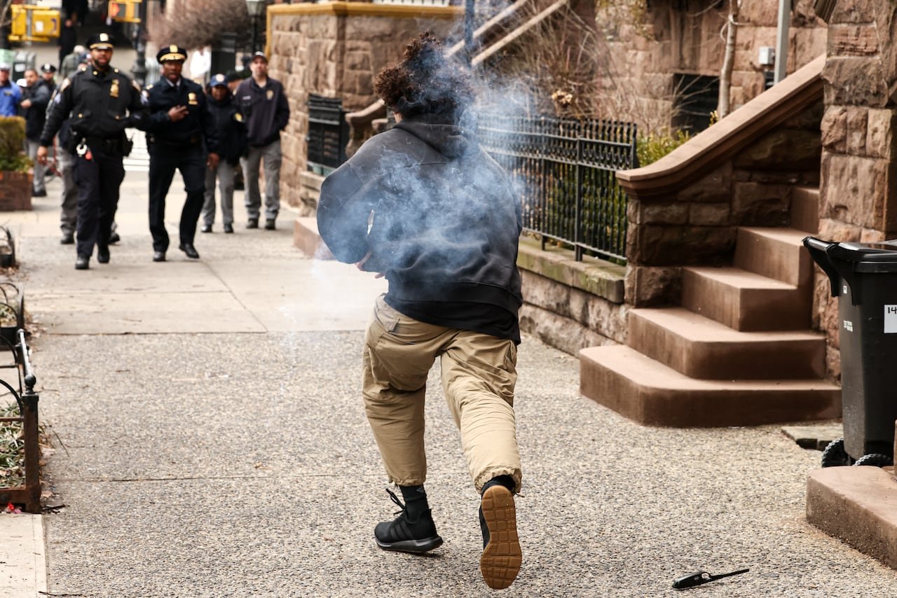 Person running while holding smoking object toward police officers