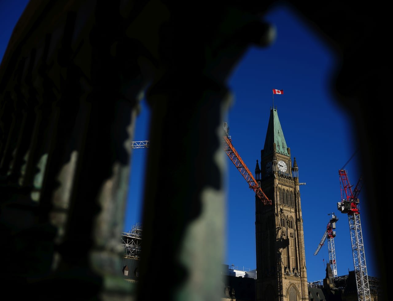 Canadian flag flying atop Parliament Hill seen through stone archway