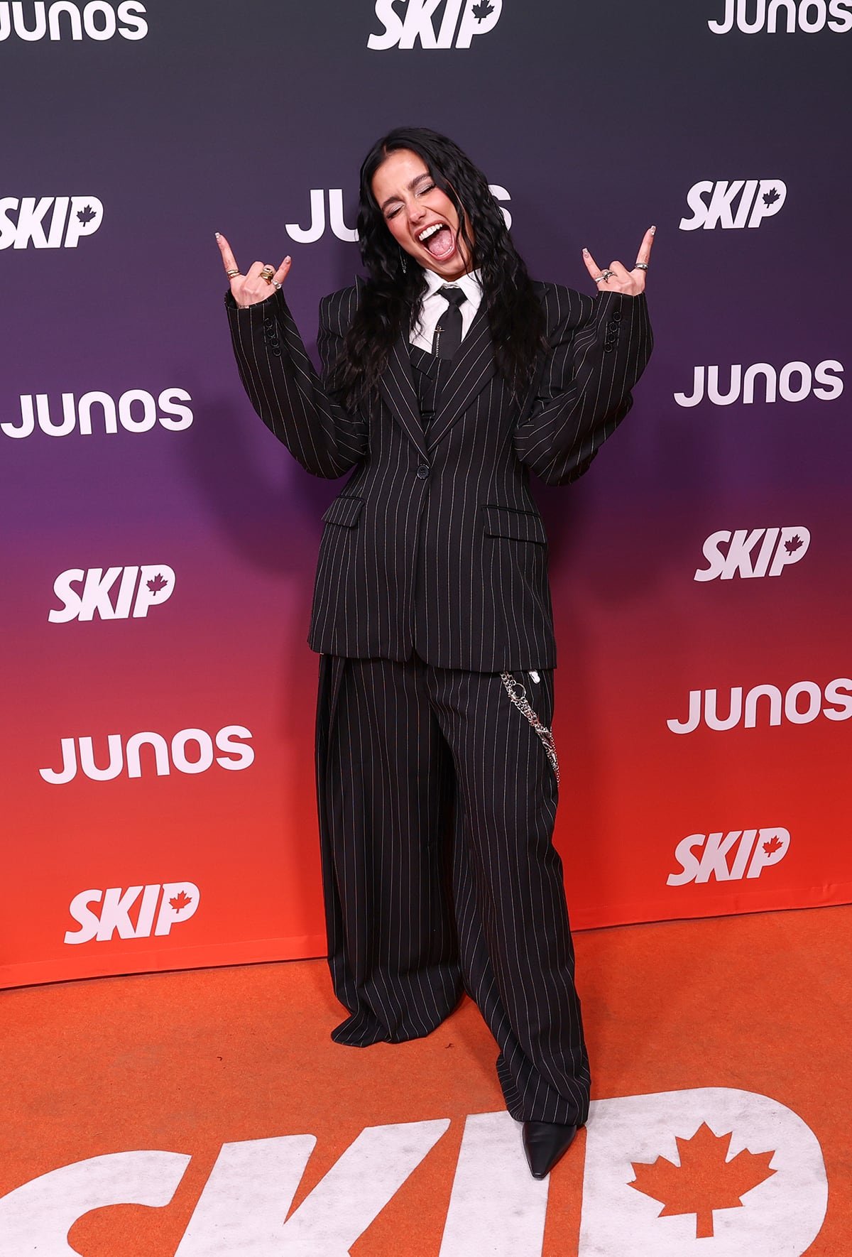 Sofia Camara wearing oversized pinstripe suit throwing devil-horn hands up
