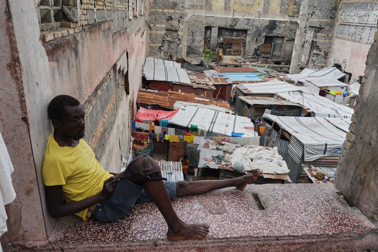 Displaced man resting outside temporary shelter after fleeing gang violence