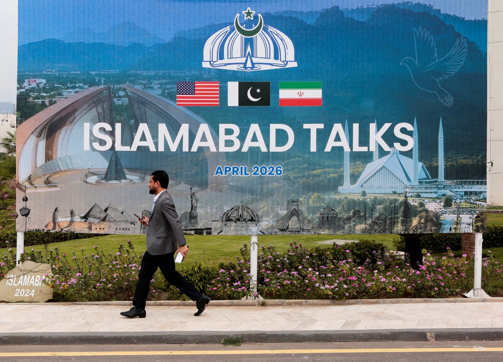 A man walking past a billboard near the media center as US and Iranian delegations prepare for peace talks in Islamabad, pakistan.