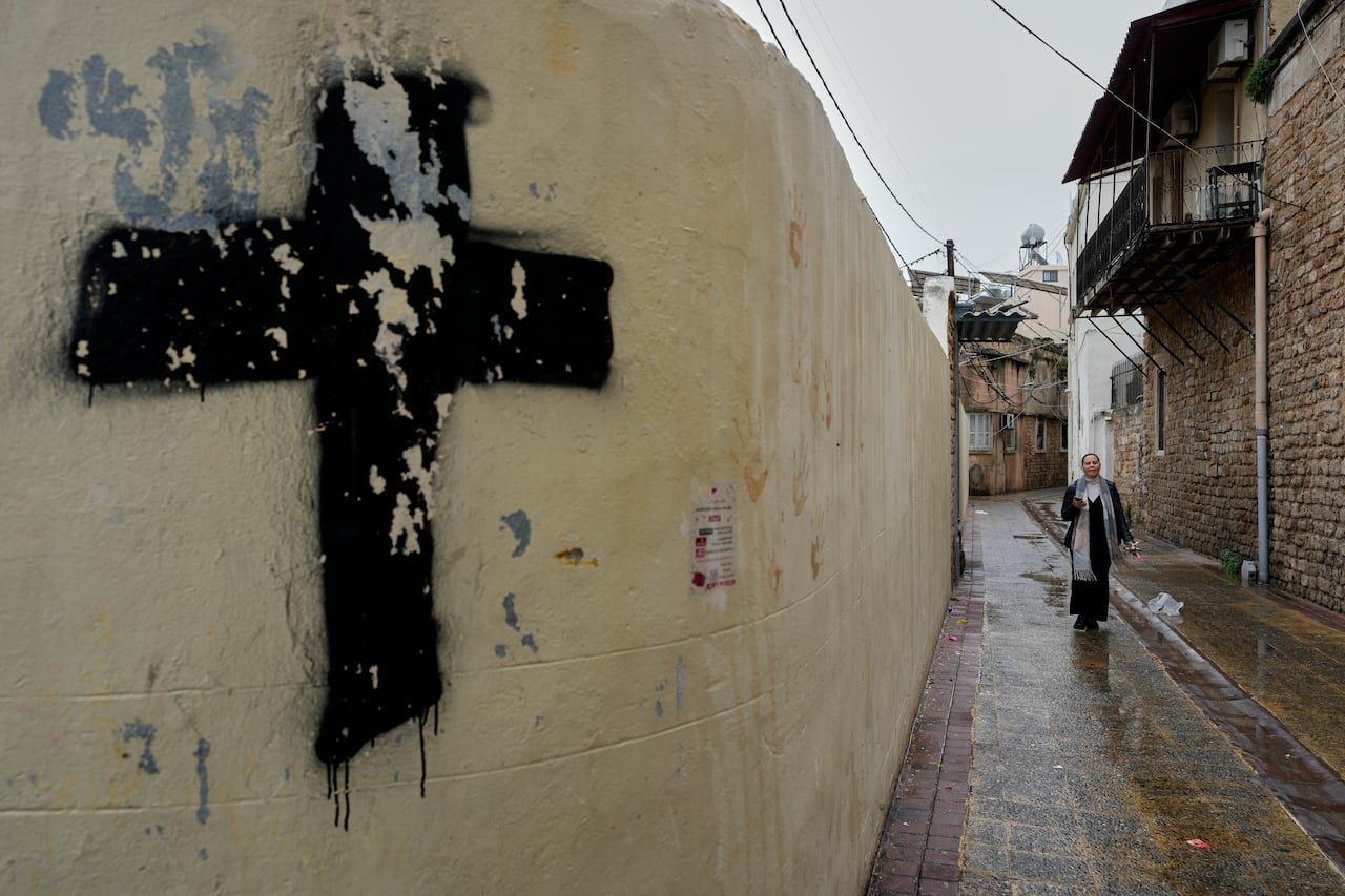 A woman walks down an alleyway painted with black cross murals