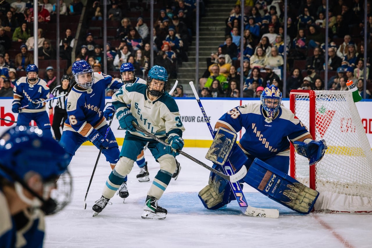 Two female hockey players competing intensely near goal crease.