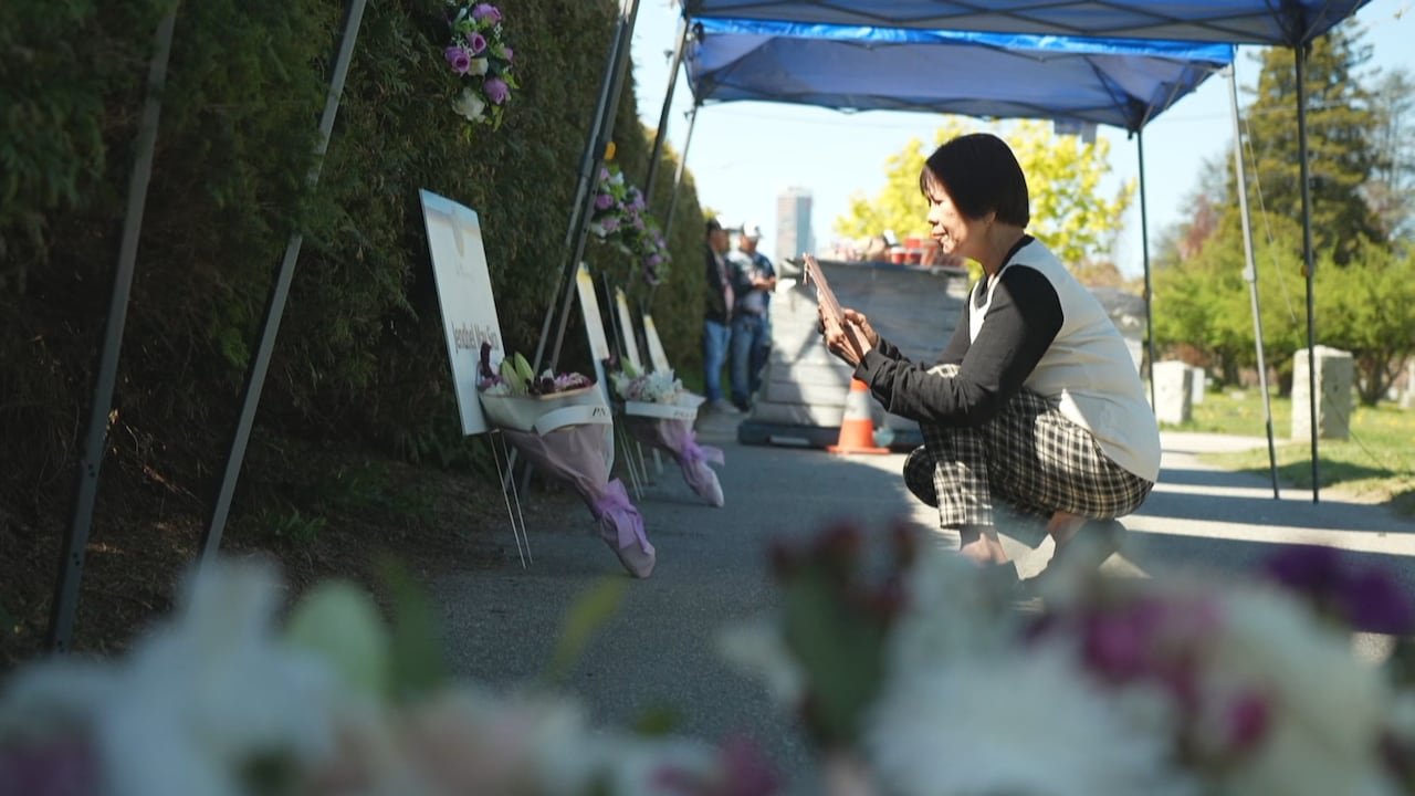 A woman kneels down before memorial displays filled with flowers.