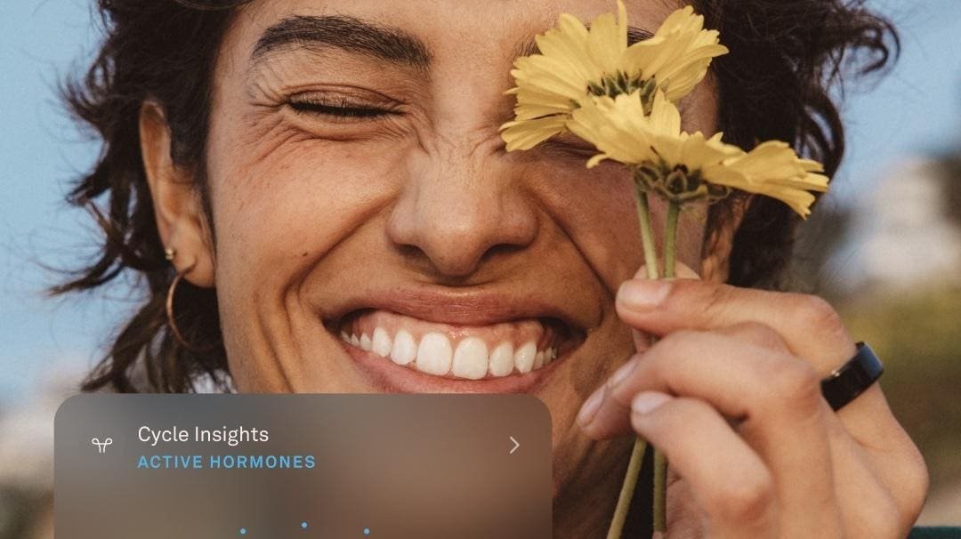 Woman smiling while holding flower near eye; interface displaying Oura app