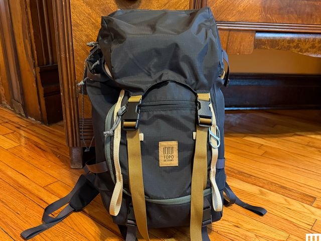 Black backpack with flap and straps on hardwood floor