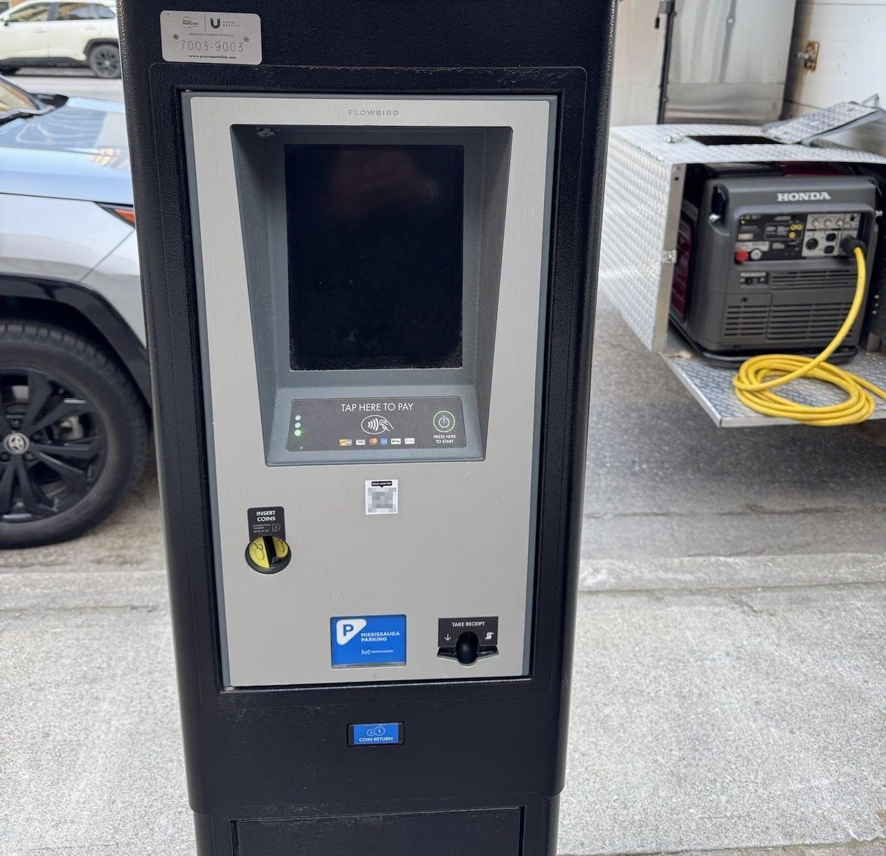 Parking machine displaying blurred-out suspicious small black-and-white faux-QR code sticker