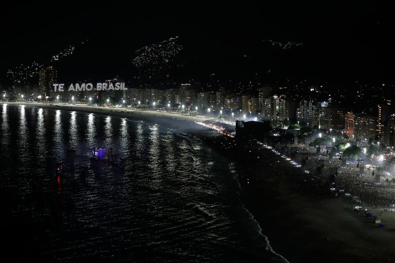 Nighttime view showing illuminated drones spelling 'I love Brazil' above packed beach audience