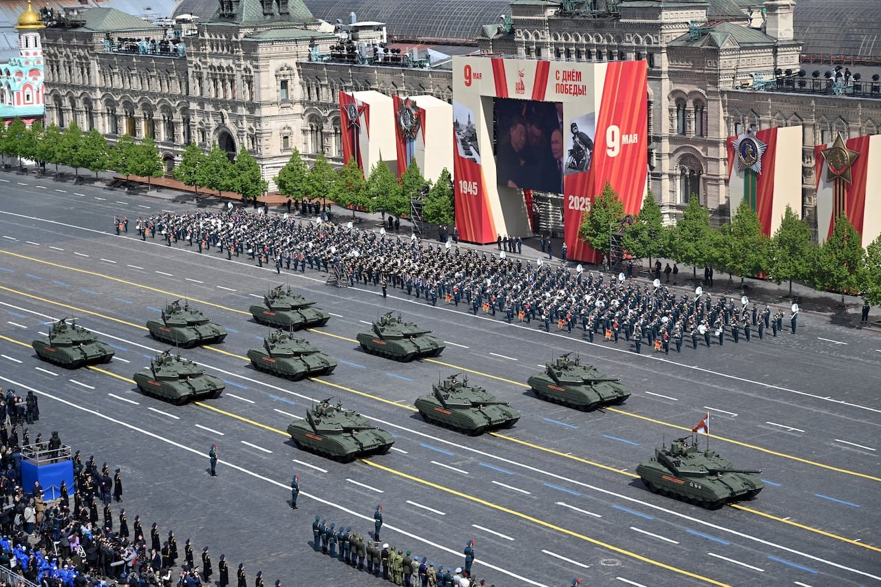 Tanks rolling down street beside marching soldiers during past parades