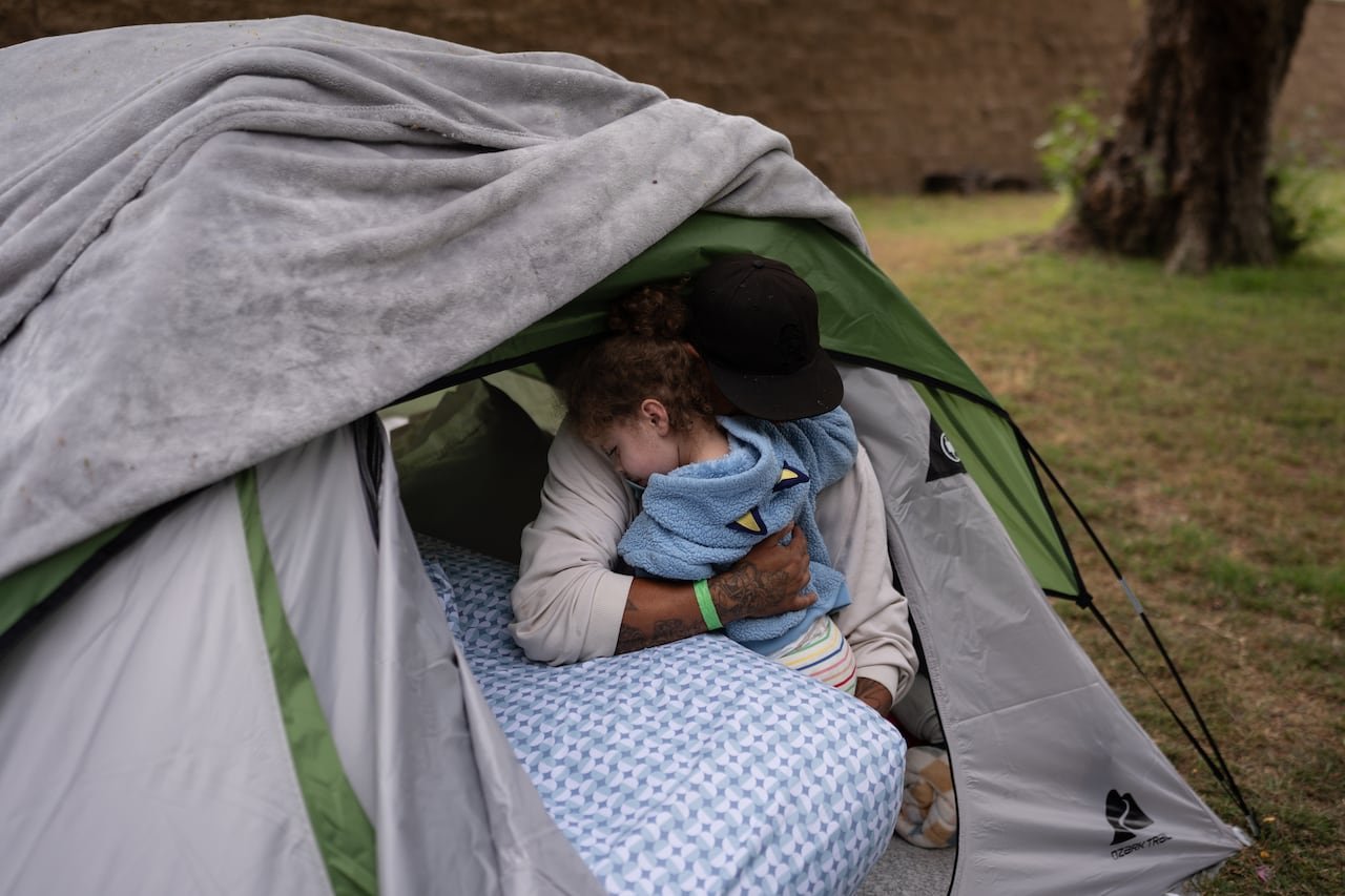 Evacuee holding child inside shelter tent