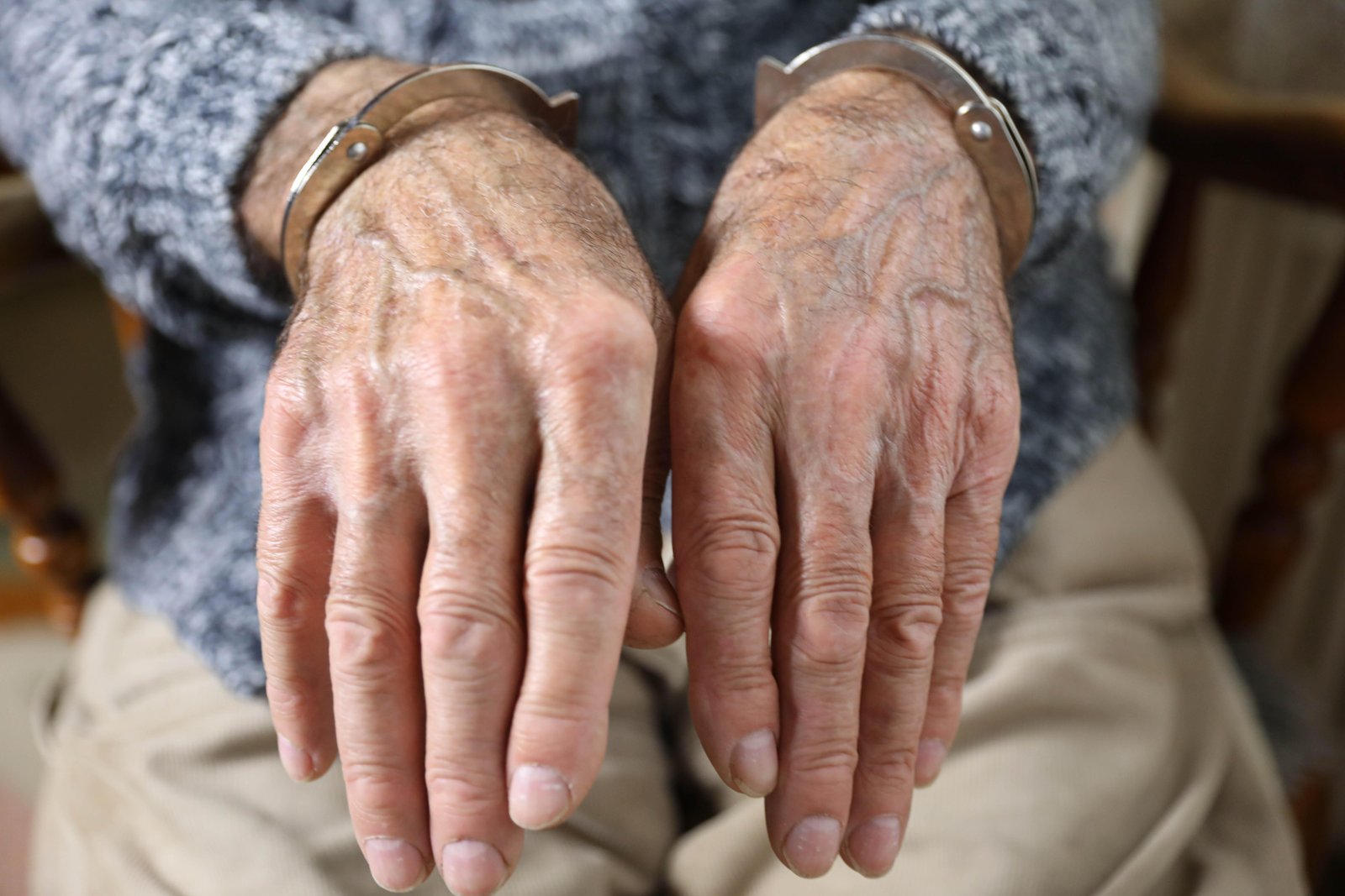Close-up image showing elderly man seated wearing handcuffs symbolizing law enforcement impact on aging