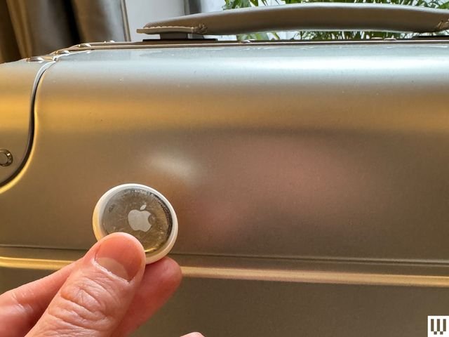 Hand holding small silver circular disc with an engraved apple logo on it