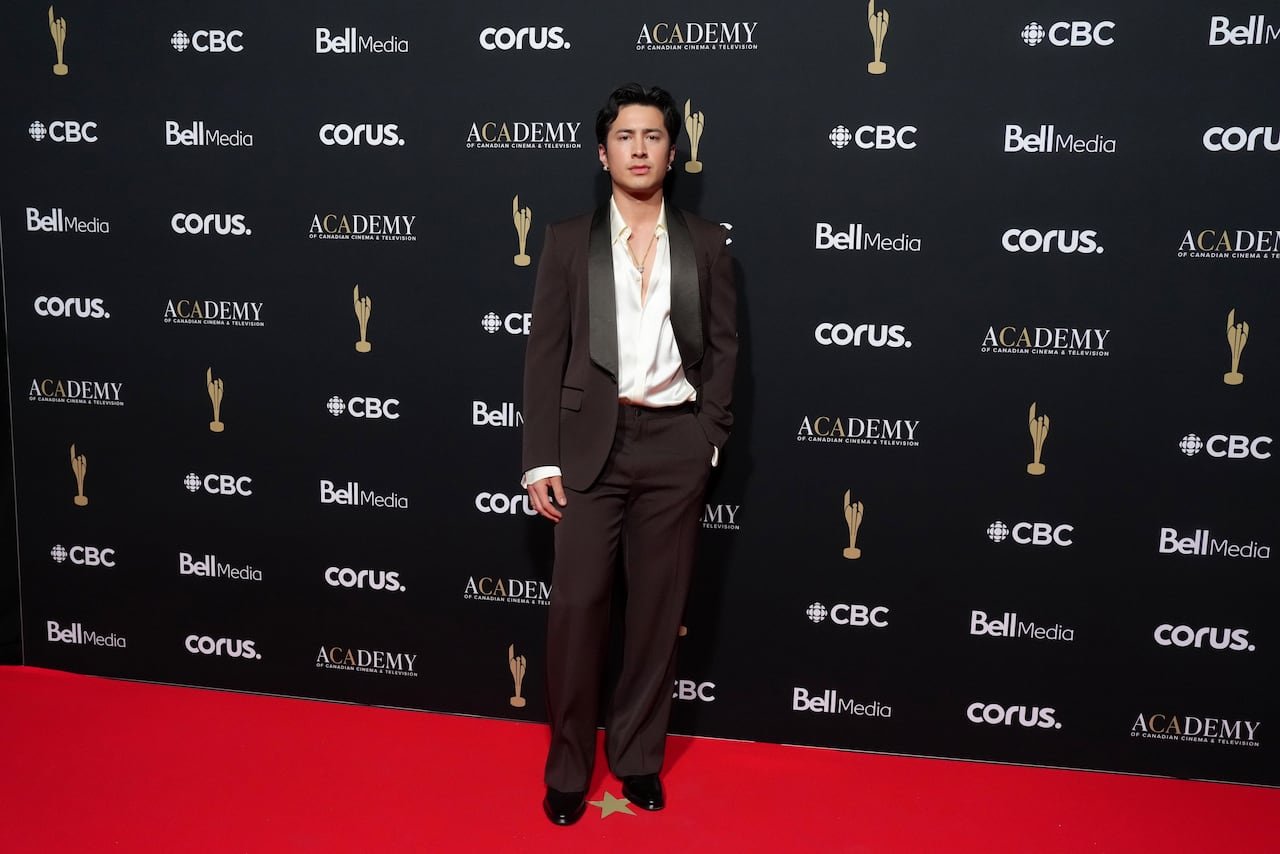 Hudson Williams posing confidently wearing dark brown tuxedo paired with white shirt unbuttoned at collar.