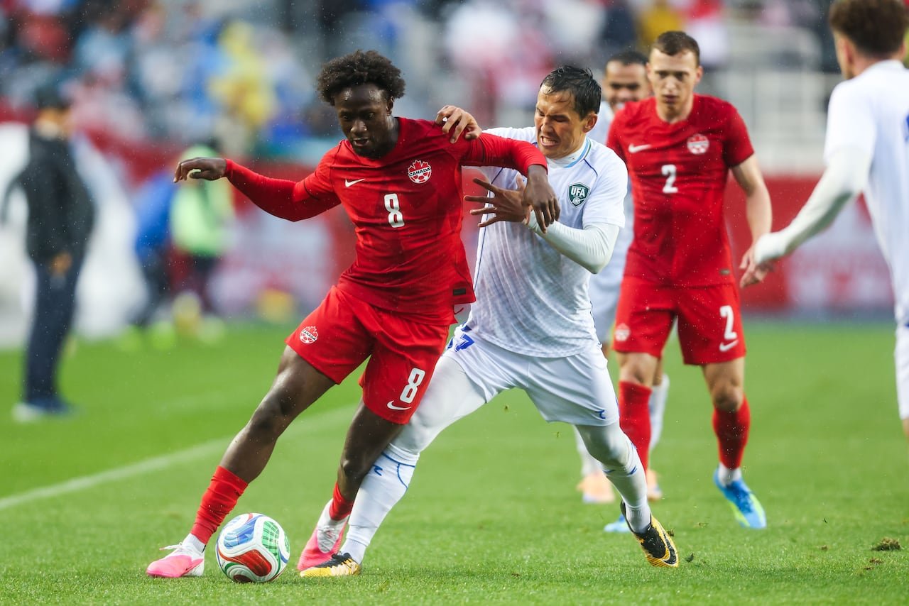 Canadian player shielding ball from opponent during rainy soccer match