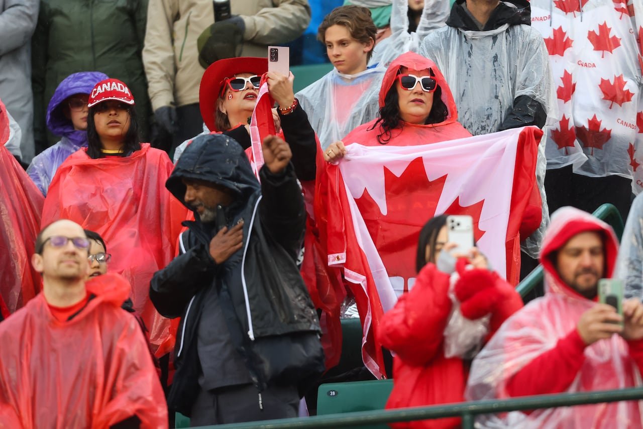 Fans wearing ponchos stand under rain during soccer game