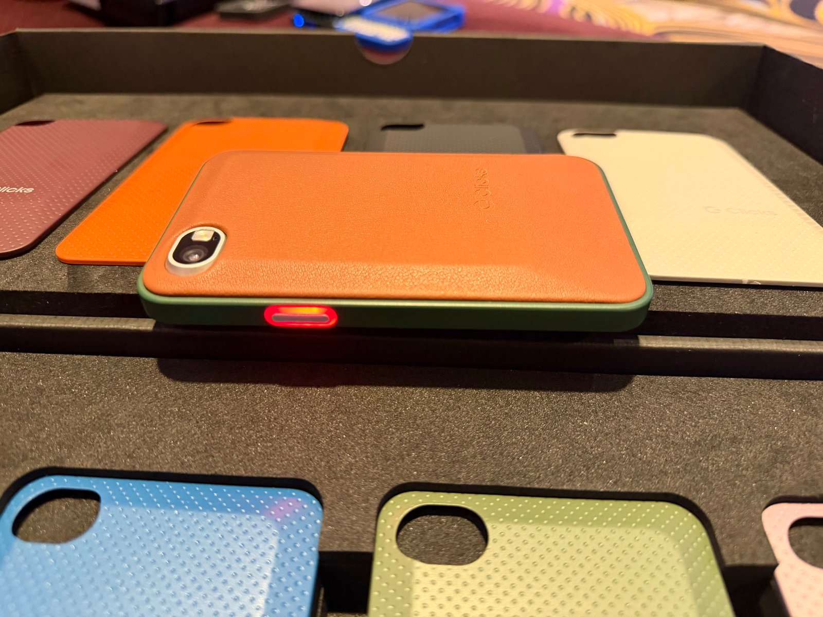 Clicks Communicator smartphone ⁤featuring orange shell and illuminated notification button.