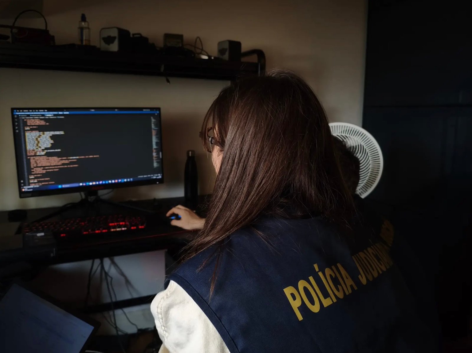European police officer inspecting computer equipment during cybercrime investigation
