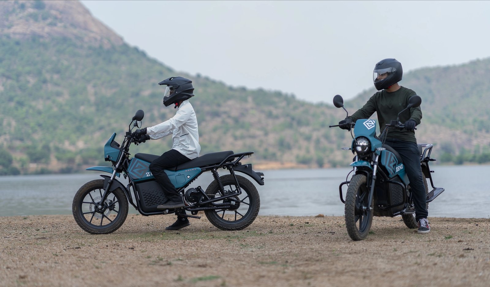 Two riders on electric motorbikes parked near a lake